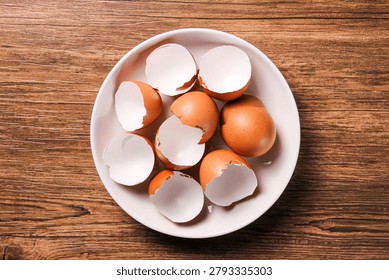 Broken eggshells in white ceramic plate on wooden table. Top view