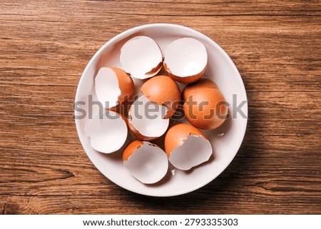 Broken eggshells in white ceramic plate on wooden table. Top view