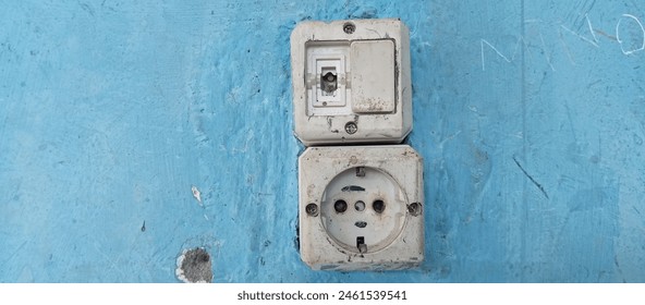 Broken electric switch and socket on blue wall