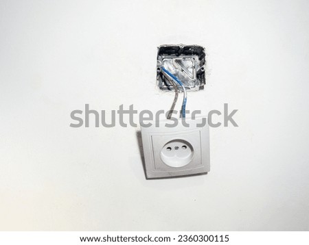 Broken electrical socket on the wall. Disassembled device. White wall with a socket pulled out of the wall. Life threatening. Broken electrical equipment concept. Appliances. Wires out. Life