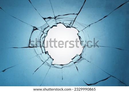 Broken glass with a hole on a blue background and with a light in the center. Texture of cracks on a broken window from explosions and gunshots.