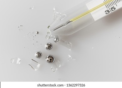 Broken glass mercury thermometer on light grey surface. Mercury drops with glass fragments. Mercury vapor poisoning.