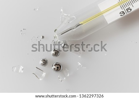 Broken glass mercury thermometer on light grey surface. Mercury drops with glass fragments. Mercury vapor poisoning.