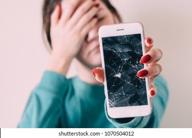 Broken glass screen smartphone in hand of upset girl, white background.
