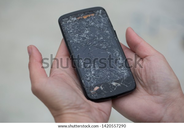 Broken glass screen smartphone in hand.Hand\
holding mobile phone with broken screen.\
Smartphone with cracked\
display in hand.Hand hold the\
cellular.