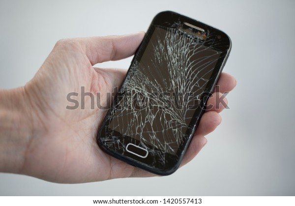 Broken glass screen smartphone in hand.Hand\
holding mobile phone with broken screen.\
Smartphone with cracked\
display in hand.Hand hold the\
cellular.