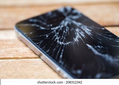 Broken glass of smart phone on the wood table. Selective focus.