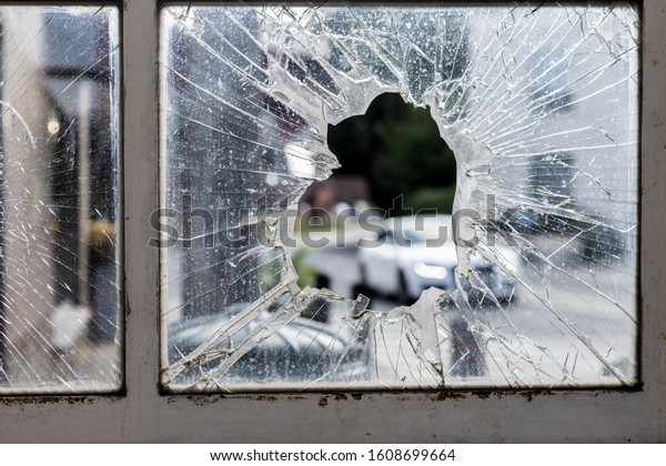 A broken glass window surrounded\
by rusty old frames with cars and a park on the\
background