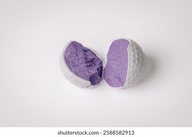 A broken golf ball split in half, exposing its purple core, placed on a white background, showing internal structure and damaged surface.