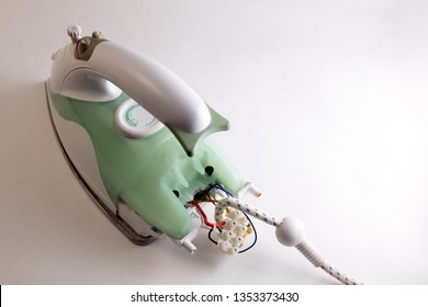 Broken Green Electric Iron With Access To The Wires And The Contact Group In The Back. Home Appliance Repair Concept. White Background. View From Above. Copy Space.