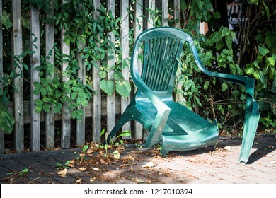 A Broken Green Garden Chair In Front Of A Fence