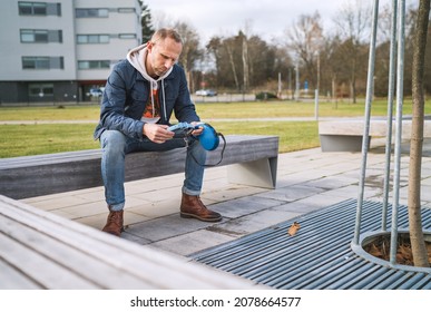 Broken With Grief Man As A Dog Owner Is Grieving Sitting On A Bench With The Lovely Pet Collar And Leash, Deep Weeping About Animal Loss. Lovely Home Pets And Sorrow Concept.