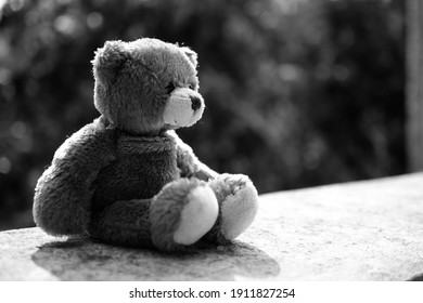 Broken heart concept. black and white image of teddy bear sad face sitting on cement wall. for isolation, loneliness, abandoned child, conceptual.
