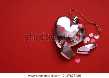 Broken heart. Crashed bauble in shape of heart with confetti on red background, top view. Space for text