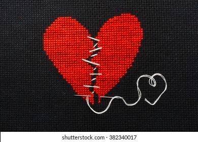 Broken heart, embroidered with red thread on black fabric. Heart sewn with white thread.