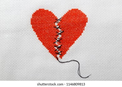 The broken heart is embroidered with red threads on a white canvas. Two halves sewn with black threads. - Powered by Shutterstock