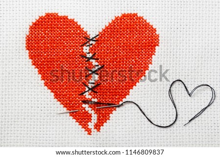 The broken heart is embroidered with red threads on a white canvas. Two halves sewn with black threads.