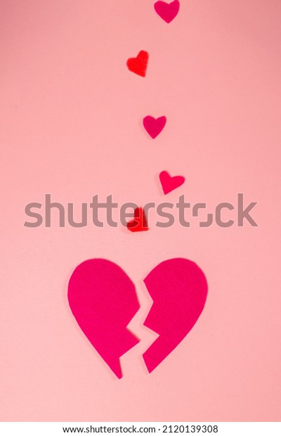 A broken\
heart. Felt heart divided into halves. Pink background, vertical\
orientation. Valentine\'s Day\
Concept.