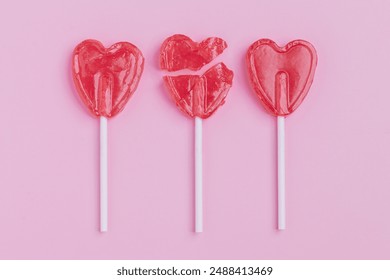 Broken heart-shaped red lollipop on a pink background. The cracked candy pieces still form a heart, creating a visually striking contrast. Ideal for themes of love, heartbreak, or Valentine’s Day. - Powered by Shutterstock