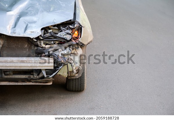 Broken hood of car on road after car accident with\
nobody copyspace. Broken car trash heap garbage. Broken Bumper and\
Car Headlights with Light On road surface asphalt with copy\
space.