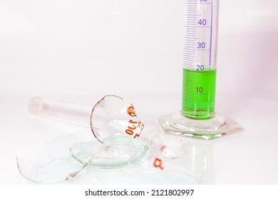 Broken Laboratory Glass, Light Liquid Chemical Spilled From Laboratory Glassware. Green Liquid In Measuring Glass. Failed Lab Experiment. Chemical Attempt.