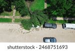 Broken large Bradford Callery pear damages parked car on residential street, suburban house front yard curbside after severe thunderstorm, Dallas, Texas, home insurance claim, storm debris aerial. USA