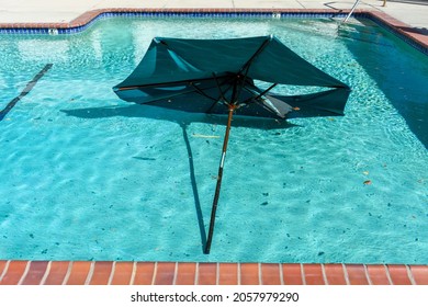 Broken Large Outdoor Umbrella Sitting At The Bottom Of The Swimming Pool After The Storm. Torn Umbrella Blown Away From The Base By Strong Wind Landed In The Water