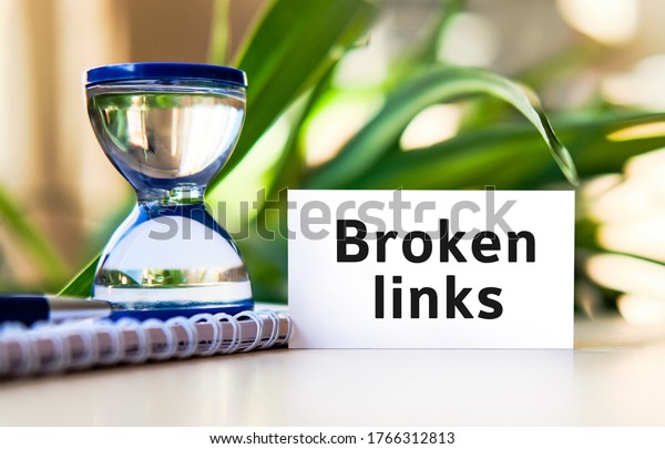 Broken links business\
concept text on a white notebook and hourglass clock, green leaves\
of flowers