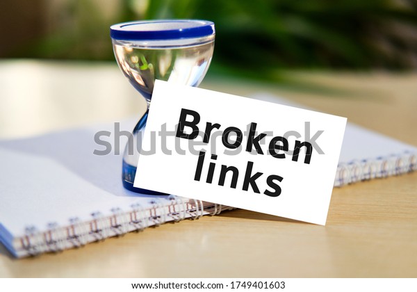 Broken links business seo\
concept text on a white notebook and hourglass clock, green leaves\
of flowers