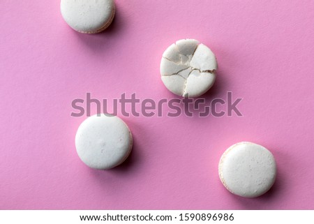 Broken macaroon cake compared to other unbroken on the pink background. The concept of non-ideality, identity; loss and broken soul