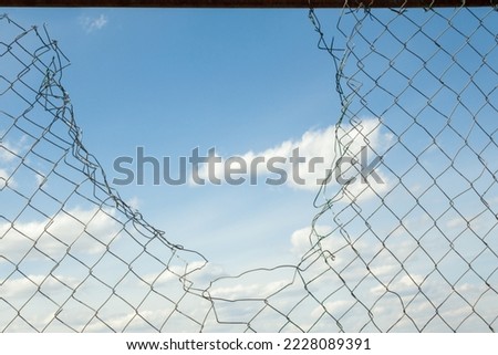 Broken metal mesh fence against the blue sky. 