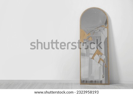 Broken mirror with many cracks near white wall indoors. Space for text