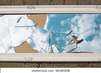 A Broken Mirror In A Vintage White Frame Lies On The Road, The Reflection Of Blue Sky And Clouds 