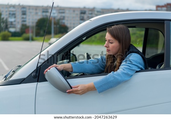 Broken off side rearview mirror on car. Driver\
woman is checking for damage on her automobile after accident.\
Transport damage, parking. Reflection glass crashed after collision\
or vandalism.