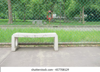 Broken Old Alone White Marble Chair In Tennis Court With Green Steel Net On Blur Park/garden/forest Trees Background