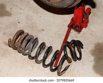 Broken Old Car Coil Spring Parts On Concrete Floor Near A Red Hydraulic Jack