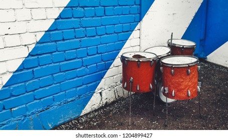 A Broken Orange Drum Set On The Street. Blue And White Color On The Wall. Telliskivi, Tallinn, ESTONIA.