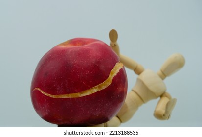 Broken overripe apple on a blurred human wooden figure background. The wooden mannequin raised his hands.