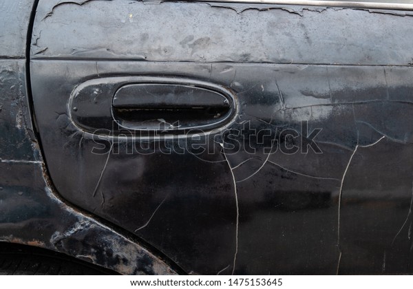 Broken part of dark black\
car body with rusty in old car.Door of the car with scratched and\
damaged paint peeled crack from the old time close up. Rust body\
car damage.