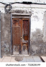 Broken Patched Old Brown Door In Rotten Frame In An Abandoned Derelict  House With Concrete Crumbling Walls Faded White Paint And Unsafe Hanging Wires