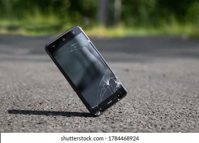 Broken phone screen on asphalt. Dropped mobile phone on the ground and smashed the screen. Falling smartphone