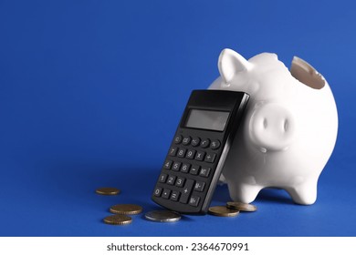 Broken piggy bank with coins and calculator on blue background - Powered by Shutterstock