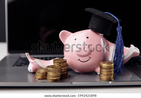 Broken piggy bank in graduation cap\
on laptop. Expensive education and scholarship\
concept