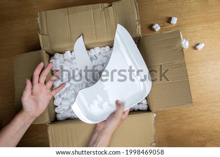 Broken plate in damaged cardboard box top view, damaged home delivery unpacking box close up