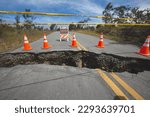 A broken road divided by a large crack from an earthquake surrounded by hazard tape and safety cones