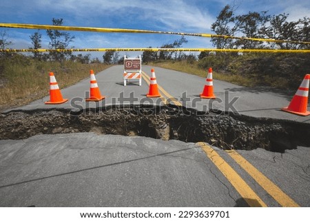 A broken road divided by a large crack from an earthquake surrounded by hazard tape and safety cones