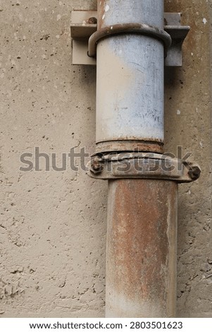 Broken rusting drain pipe mounted to a concrete pillar.