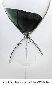 Broken sandglass with black sand leaking out