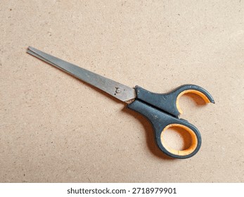Broken scissors with cracked plastic handle isolated on brown background, showing damaged cutting tool condition, worn metal blades, safety risk, and repair concept