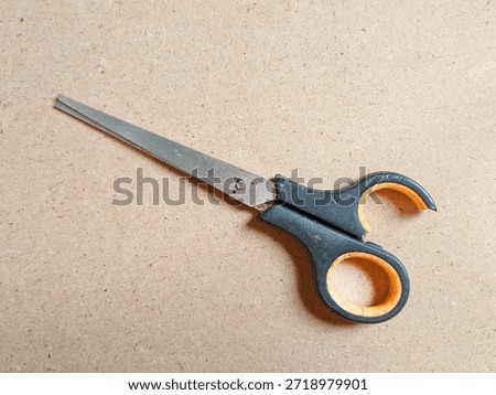 Broken scissors with cracked plastic handle isolated on brown background, showing damaged cutting tool condition, worn metal blades, safety risk, and repair concept